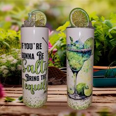 two tumblers with limes on them sitting next to some flowers and plants in the background