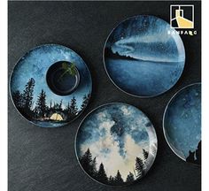 four plates with trees on them sitting on a black counter top next to each other