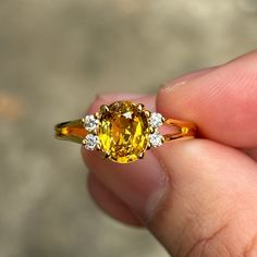 a close up of a person's hand holding a ring with an orange and white diamond