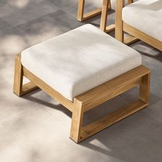 two wooden benches with white cushions sit on the cement floor next to each other in front of a tree