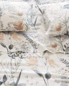 a bed with two pillows on top of it next to a pillow case that has flowers and leaves printed on it