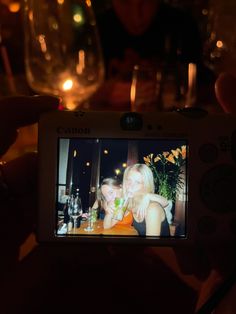 a person taking a photo with a camera in front of some wine glasses and candles