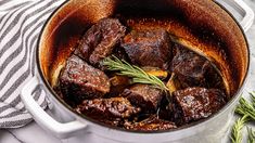 a pot filled with beef and potatoes on top of a table next to a striped towel