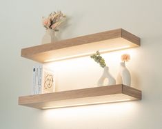 two white vases sitting on top of wooden shelves next to each other with flowers in them