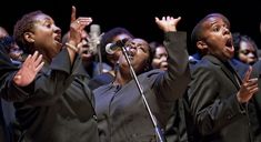 a group of people singing into microphones in front of a crowd with their hands up