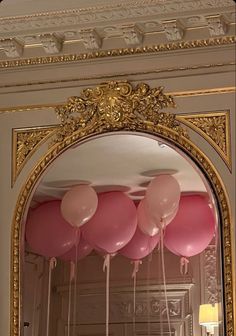 pink balloons are floating from the ceiling in front of an ornate gold framed mirror with golden trim