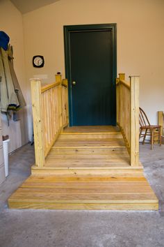 a wooden porch with steps leading up to a green door and clock on the wall