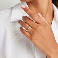 a woman wearing a white shirt and a gold ring on her left hand with a diamond set in the middle