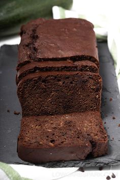 a loaf of chocolate cake sitting on top of a cutting board next to cucumbers