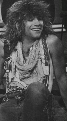 a black and white photo of a man with long hair wearing a cowboy hat sitting on a bench