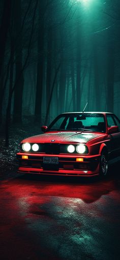 a red car parked in the middle of a dark forest at night with headlights on