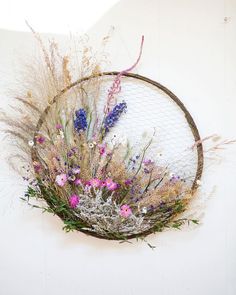 an arrangement of wildflowers and grasses in a wire basket on a white wall