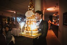 a man in a tuxedo is holding a cake with lit candles on it