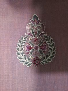 an embroidered brooch is sitting on a purple cloth