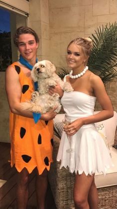 a man and woman dressed up as flint and the flintstones, holding a dog