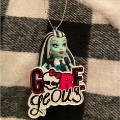 a necklace with an image of a doll hanging from it's side on a black and white checkered surface