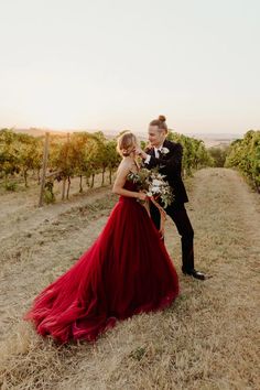 a man and woman in formal wear standing next to each other on a vineyard field