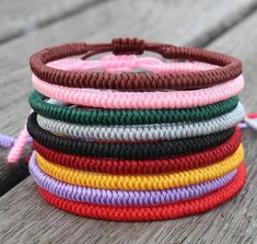 a stack of multicolored bracelets sitting on top of a wooden table next to a tassel