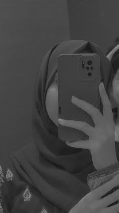 a woman taking a selfie with her cell phone in front of her face while wearing a hijab