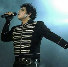 the singer is dressed in black and gold with his microphone up to his ear as he sings