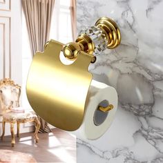 a gold toilet paper holder hanging from the side of a white marble bathroom wall next to a chair