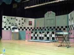 an empty stage with chairs and tables in front of a black and white checkered wall