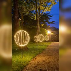 lighted orbs in the grass on a path at night with trees and lights behind them