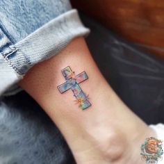 a cross tattoo on the ankle with flowers and leaves around it's center piece