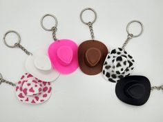 four different colored hats are attached to key chains on a white surface with black, pink, and white polka dots