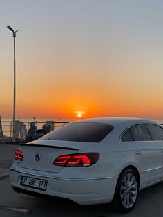 a white car is parked in the parking lot as the sun sets over the water