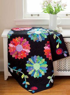 a black quilted blanket with colorful flowers on it next to a window sill