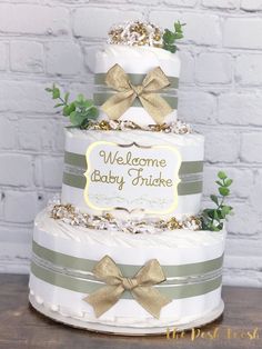 a three tiered cake with bows and welcome baby sign on the top, sitting on a wooden table