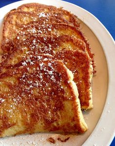 two pieces of french toast on a white plate with powdered sugar over them and blue table cloth