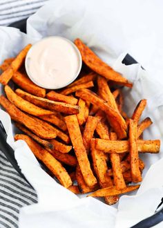 french fries with dipping sauce in a basket on a striped cloth next to a napkin