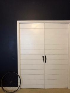 a bike leaning against the wall in front of two white garage doors with black handles