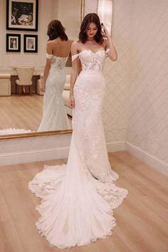 a woman standing in front of a mirror wearing a wedding dress with an off the shoulder neckline