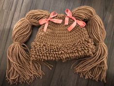 a brown crocheted hat with pink bows on the front and back, sitting on top of a wooden floor