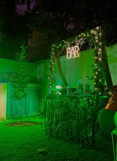 an outdoor bar set up at night with green lights and decorations on the grass in front of it