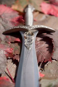 a pair of wedding rings sitting on top of a knife in the middle of leaves