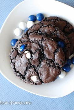 two chocolate cookies with white and blue candies are on a plate next to a glass of milk