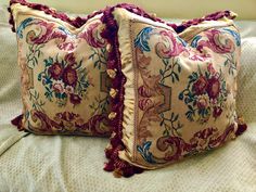 two decorative pillows sitting on top of a bed