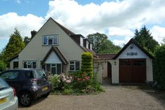 two cars parked in front of a house with flowers on the driveway and bushes around it