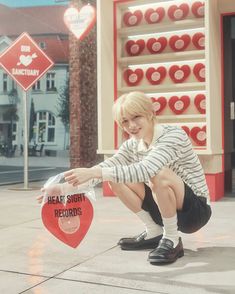 a woman kneeling down next to a heart shaped box on the ground in front of a store