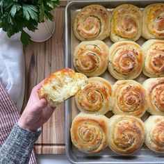 a person holding a piece of bread in front of a pan filled with rolls on a cutting board