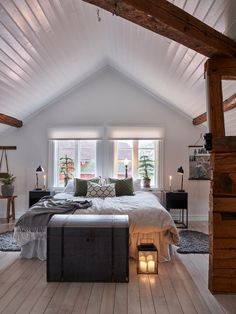 an attic bedroom with white walls and wood flooring is lit by two candles on the bed