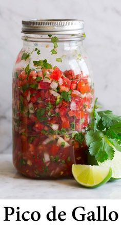 a jar filled with lots of food next to a lime and some cilantro