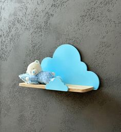 a blue cloud shaped shelf with a teddy bear on it's side, against a gray wall