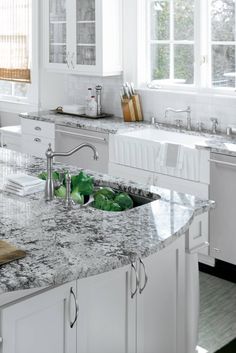 a kitchen with marble counter tops and white cabinets, along with an island in the middle