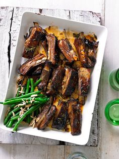 a white plate topped with meat and green beans next to two glasses on a wooden table