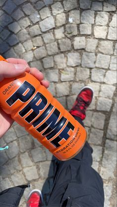 a person holding an orange drink in front of their feet on a cobblestone walkway